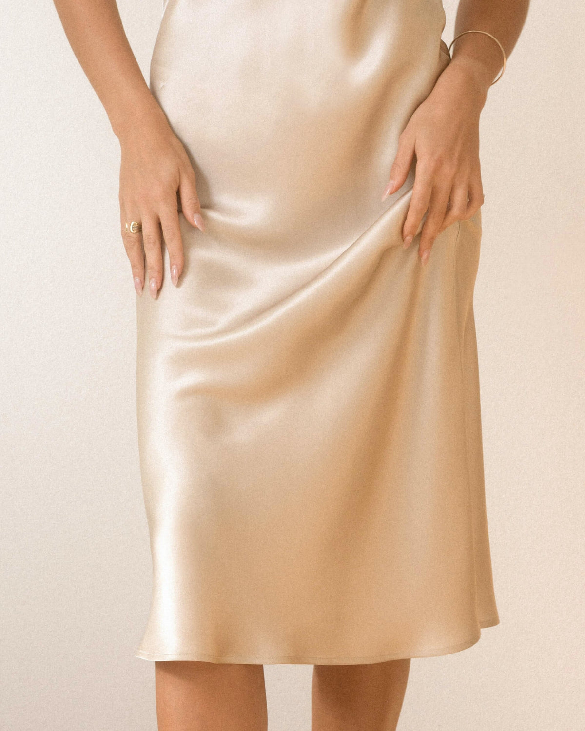 Detalje af silkens glans og bløde fald på Isadora lang silkenatkjole i champagne, vist på en model.