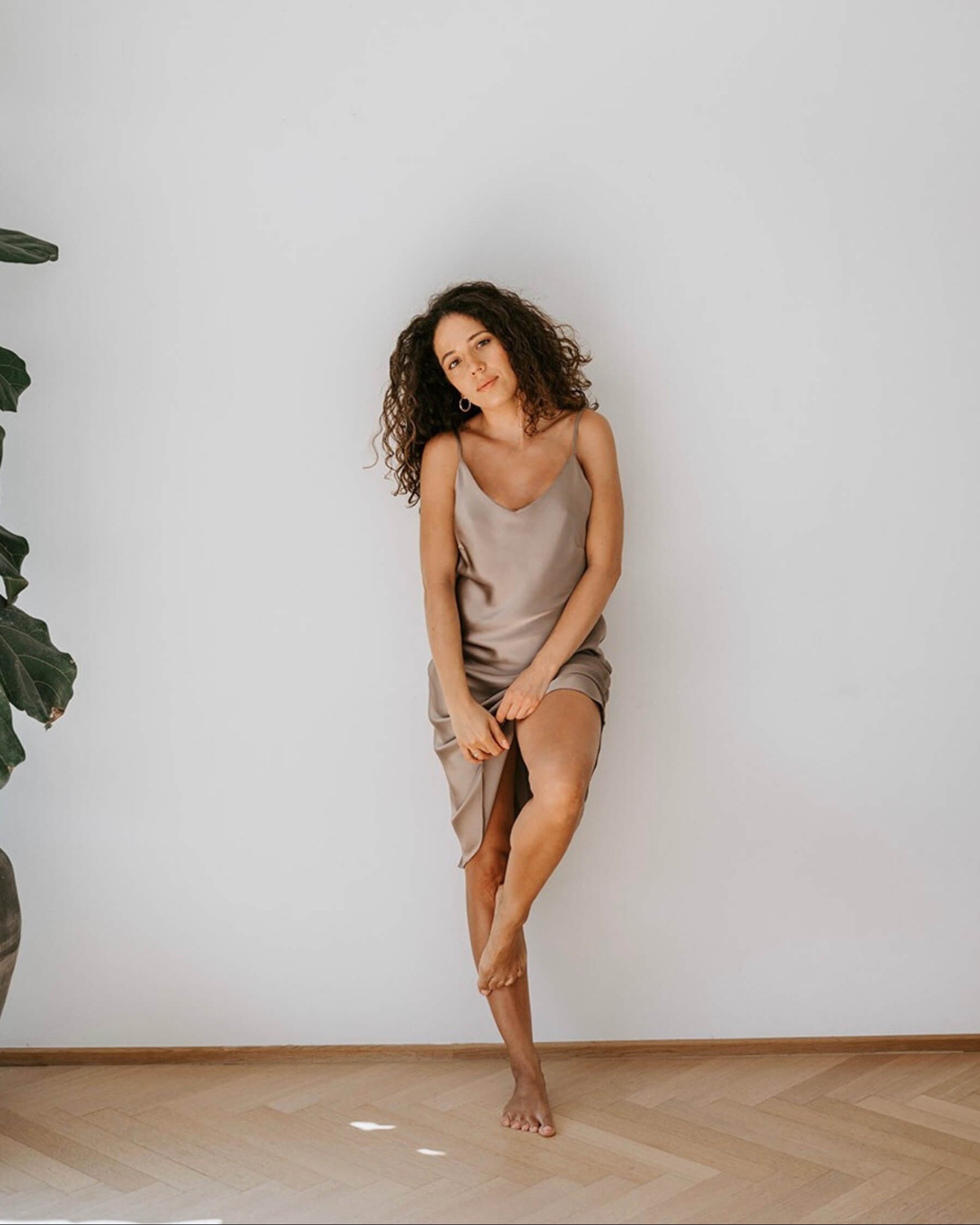 Kvinde iført silkenatkjole i rosa mulberry silke, stående i et lyst minimalistisk rum.