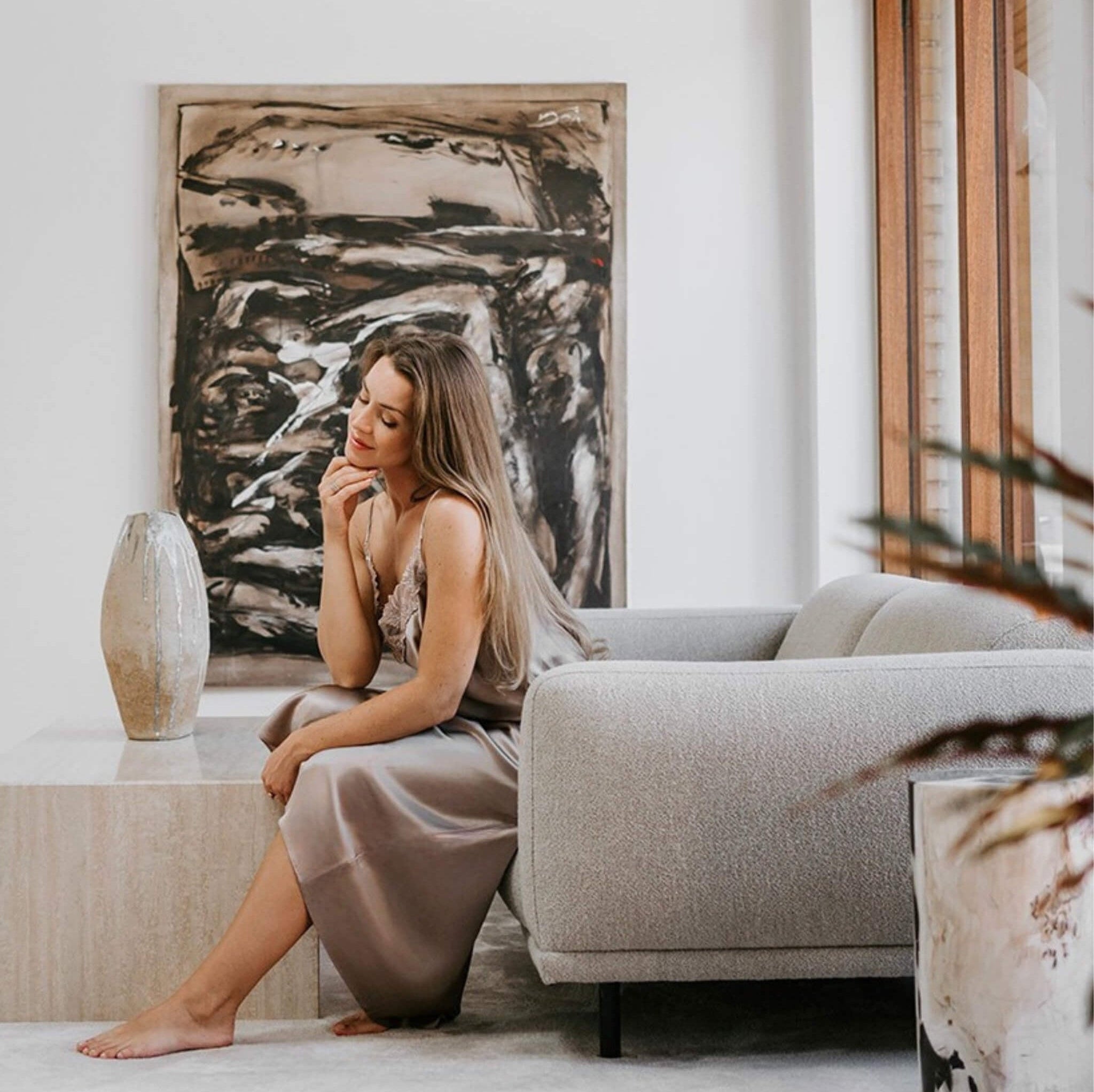 Kvinde i støvet rosa silkenatkjole fra Marimi siddende i et skandinavisk, minimalistisk rum - ro, kvalitet og tidløs design.